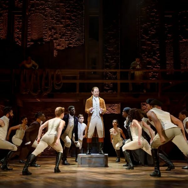 Cena do musical Hamilton na Broadway, mostrando os atores em figurinos de época durante uma das performances musicais deste revolucionário musical da Broadway