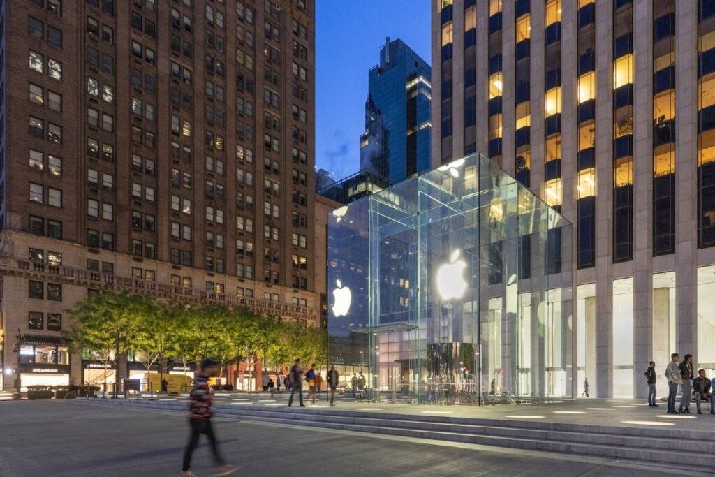 A modern glass facade adorns the iconic Apple Store on 59th Street, its sleek design gleaming under the warm glow of natural daylight. Passersby pause to admire the latest tech marvels showcased in the store's pristine window displays. Inside, clean lines and minimalist decor create an atmosphere of sophistication, inviting visitors to explore the latest innovations in consumer electronics. The store's upper levels offer breathtaking views of the bustling streets below, with guests capturing memorable shots on their iPhone cameras. This temple of technology stands as a testament to Apple's commitment to elegant design and seamless user experience, making it a must-visit destination on the famous Fifth Avenue. A Apple Store da Quinta Avenida é um dos principais pontos de Compras de Nova York