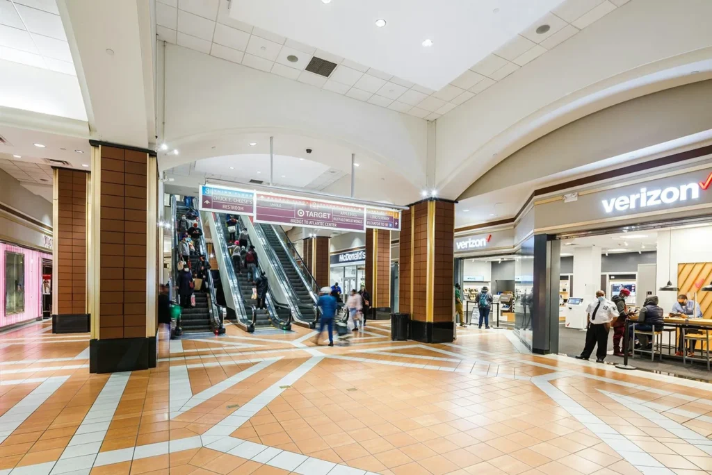A bustling city street in New York City, with towering high-rises and iconic skyscrapers in the background, illuminated by warm golden light. In the foreground, a sprawling shopping mall with a grand, modern facade and large glass windows displaying the latest fashion trends. Shoppers stroll along the well-maintained walkways, carrying shopping bags and enjoying the vibrant atmosphere. The scene exudes a sense of energy and excitement, capturing the essence of the premier shopping destinations that lie beyond the confines of Manhattan. Atlantic Terminal Mall, centro de compras no Brooklyn, Nova York