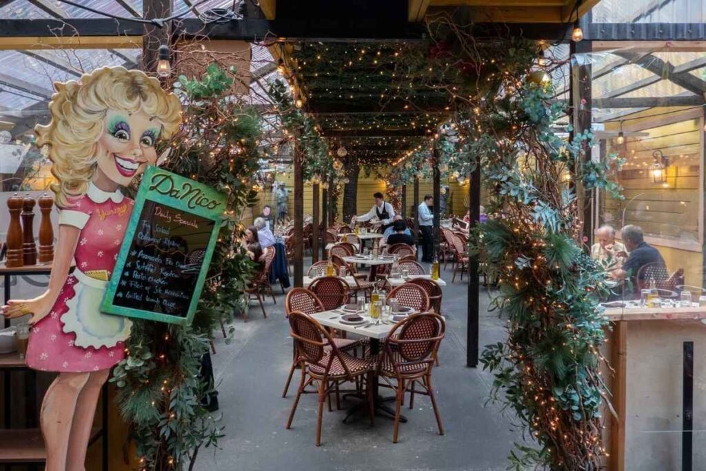 A bustling outdoor market in the heart of Little Italy, with vibrant stalls offering an array of local delicacies beyond just Italian fare. Weathered brick buildings line the cobblestone streets, casting warm shadows over the scene. Sunlight filters through the canopies, illuminating the diverse selection of handcrafted goods, from fragrant spices to artisanal baked treats. In the foreground, a group of locals and tourists mingle, their laughter and conversation creating a lively atmosphere. The middle ground showcases the diverse culinary offerings, from steaming tamales to fresh-squeezed juices. The background reveals a glimpse of the neighborhood's historic architecture, hinting at the cultural tapestry that extends beyond the familiar Italian influence. Restaurante Da Nico