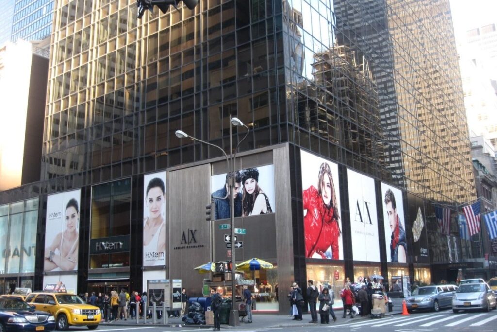 Quinta Avenida Nova: a vibrant, bustling street with towering skyscrapers, high-end boutiques, and chic cafes. The sun casts a warm glow, illuminating the intricate architecture and the well-dressed crowds strolling along the sidewalks. In the foreground, elegant window displays showcase the latest fashion and luxury goods, inviting passersby to explore. The middle ground features a lively mix of pedestrians, luxury vehicles, and street performers, creating a dynamic energy. In the background, the skyline rises, a symphony of glass and steel, reflecting the power and affluence of this iconic shopping district. compras na quinta avenida