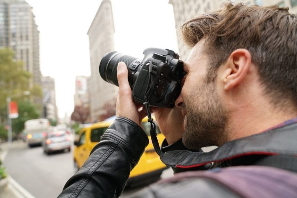 A bustling New York City cityscape, featuring iconic skyscrapers and landmarks, captured through the lens of a professional-grade camera. In the foreground, a high-quality DSLR camera with a wide-angle lens stands ready, its sturdy tripod firmly planted on the sidewalk. The photographer, clad in a casual yet refined outfit, is carefully framing the shot, adjusting the settings to account for the dramatic lighting and architectural details. The middle ground showcases the towering Empire State Building, its Art Deco spire reaching towards the sky, while the background is filled with a mix of classic and contemporary structures, each with their own unique character and aesthetic. The overall scene conveys a sense of focused creativity, capturing the essence of the city's iconic buildings through the lens of a skilled photographer. fotografando em de nova york