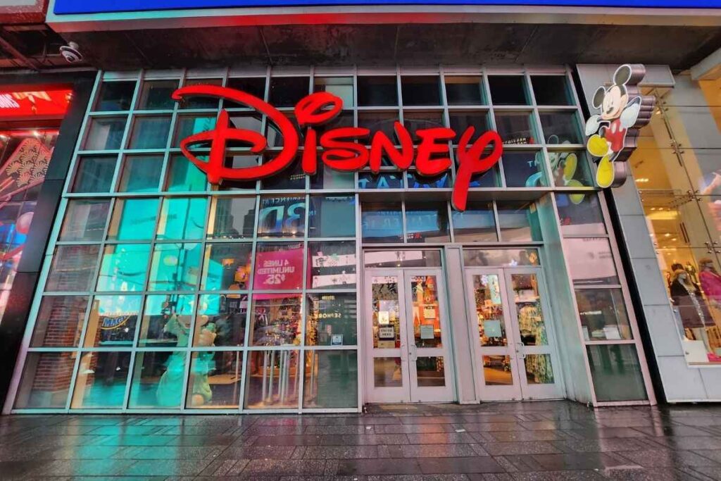 A vibrant bustling street in New York City, with a diverse array of shops, boutiques, and department stores lining the sidewalks. Shoppers from all walks of life navigate the crowded streets, bags in hand, admiring window displays and ducking into enticing storefronts. Skyscrapers tower overhead, casting long shadows that create a sense of scale and grandeur. The scene is bathed in warm, golden afternoon light, capturing the energy and excitement of a prime shopping destination. The overall atmosphere conveys the thrill of exploring the countless retail options that make New York a shopper's paradise. Loja da Disney na Times Square