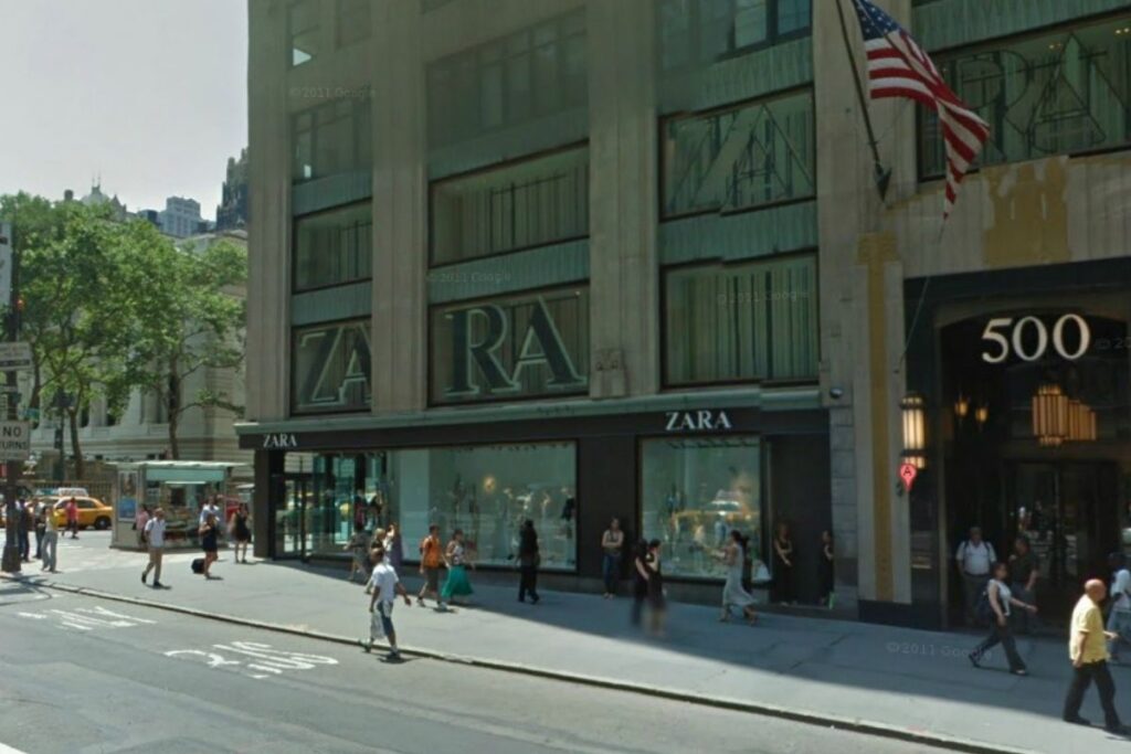 A bustling cityscape of New York's Fifth Avenue, showcasing the iconic storefront facades of Uniqlo, Zara, H&M, and GAP. Pedestrians stroll past the vibrant, modern displays in an atmosphere of dynamic energy and urban sophistication. Warm, diffused lighting illuminates the scene, casting a golden glow on the sleek glass and steel exteriors. The middle ground features the well-dressed crowds navigating the sidewalks, while the background frames the towering skyscrapers that define the Manhattan skyline. An inviting, accessible shopping experience captured in a visually striking, cinematic composition. Zara na Quinta Avenida