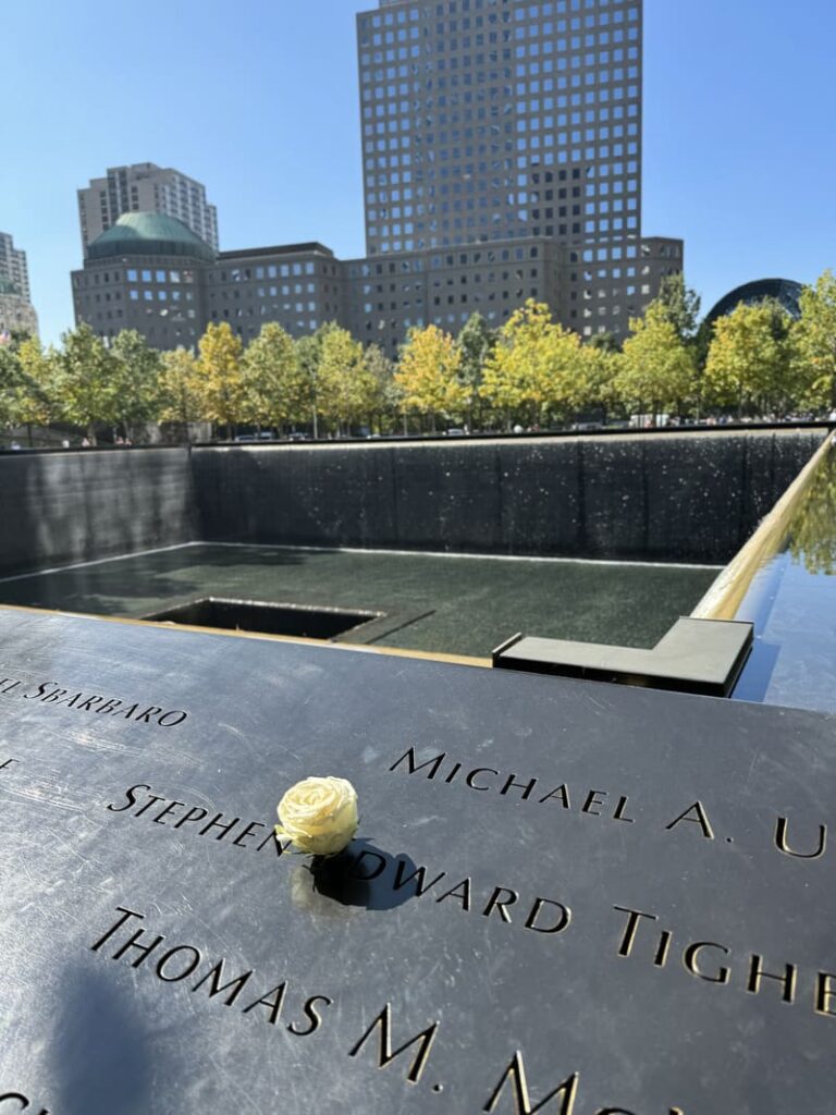 Vista ampla da Piscina do Memorial 11/09 com uma rosa branca colocada em nome de uma vítima, foto autoral capturando a homenagem na visita.