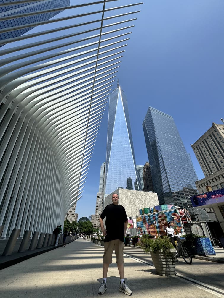 Autor do artigo ao lado da Estação Oculus com o One World Trade Center ao fundo, registrando a experiência no centro de transporte de Nova York, foto autoral.