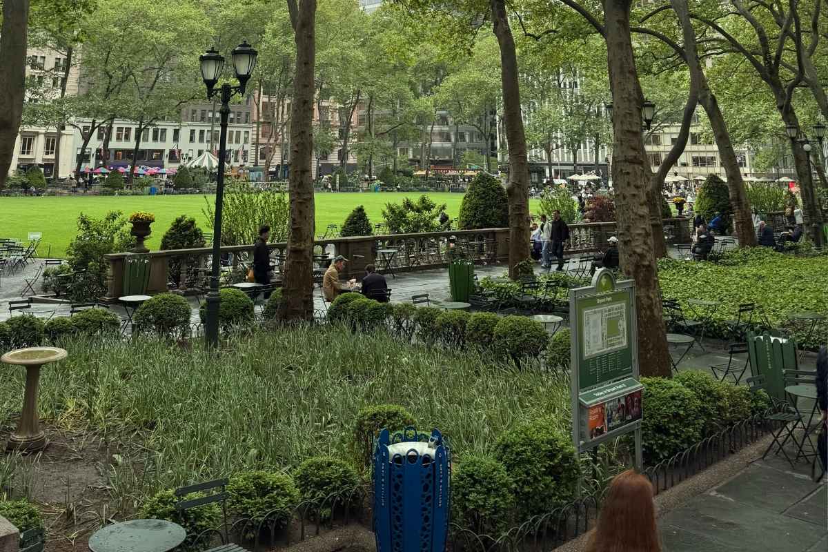 Pessoas estudando ao ar livreno Bryant Park em Nova York, com árvores, flores, bancos e prédios da cidade ao fundo. foto autoral