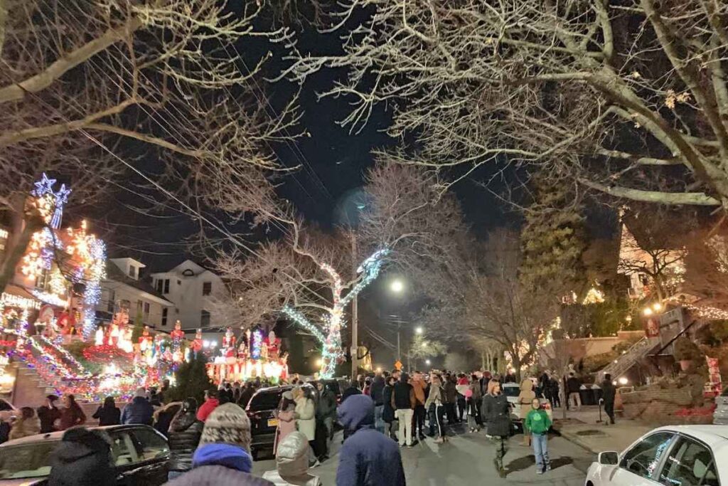 Rua residencial decorada com luzes de Natal coloridas, pessoas caminhando