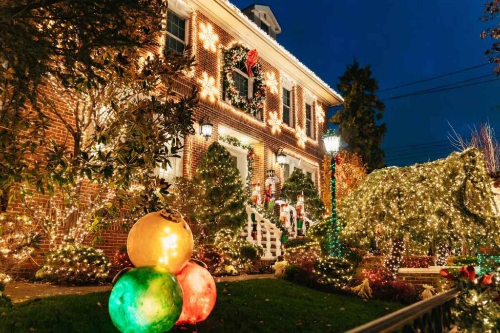 Rua residencial iluminada com decorações natalinas coloridas em Dyker Heights à noite.